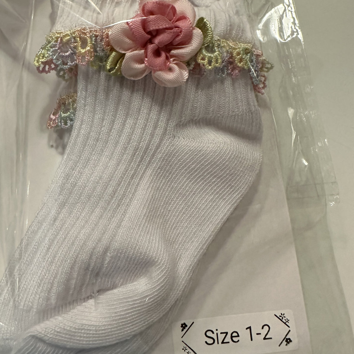 White baby cotton socks with pale rainbow lace trim and flower.