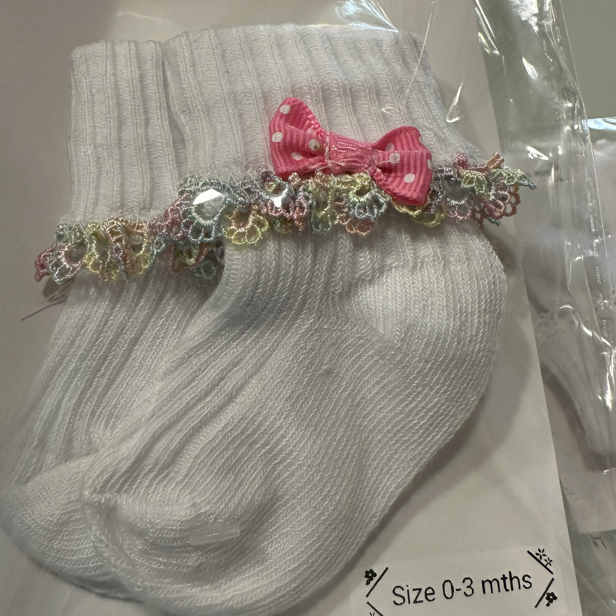 White baby cotton socks with pale rainbow lace trim and bow.