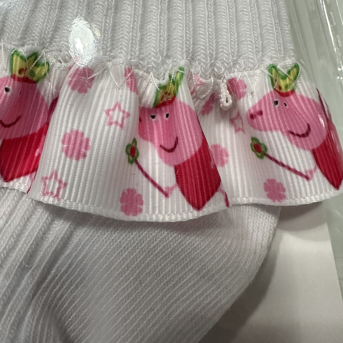 Close up of White baby cotton socks with pepper pig ribbon trim.
